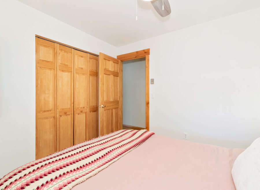 This bedroom features a large bed with a pink comforter and a colorful striped throw blanket.