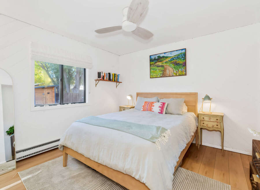 This charming bedroom features a comfortable queen-size bed with crisp white linens and a light blue throw blanket.