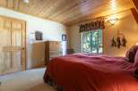 Experience rustic charm in this cozy bedroom, featuring a warm wooden ceiling and a large window offering serene forest views.