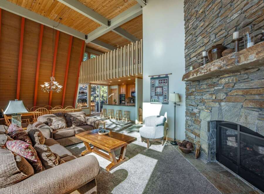 Experience rustic charm in this spacious living area, featuring a soaring wood-paneled vaulted ceiling with exposed beams and striking orange accents.