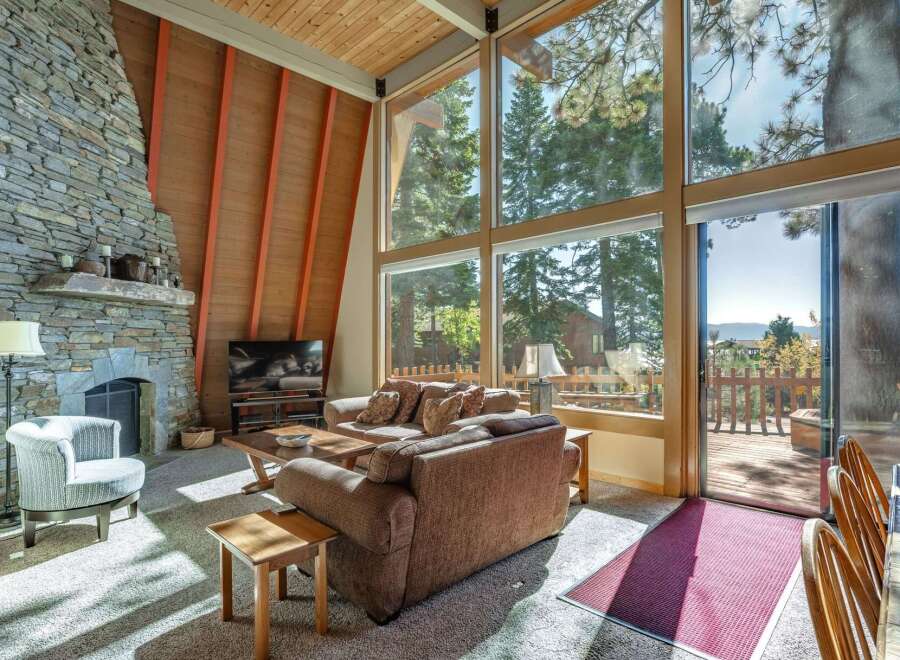 Experience breathtaking mountain views from this stunning living room, featuring a grand stone fireplace and expansive floor-to-ceiling windows.