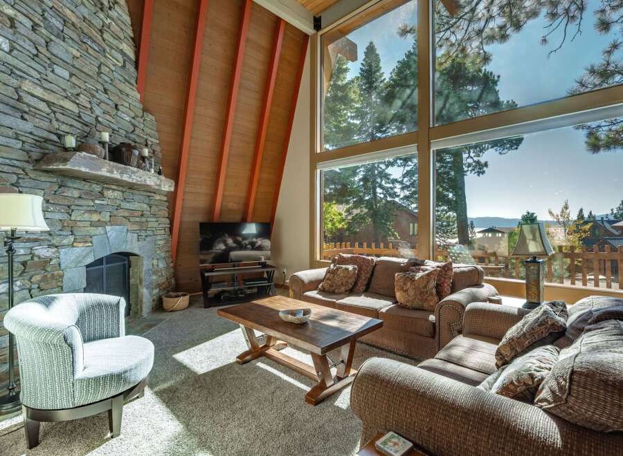Experience breathtaking mountain views from this stunning living room, featuring a grand stone fireplace and soaring A-frame ceilings.