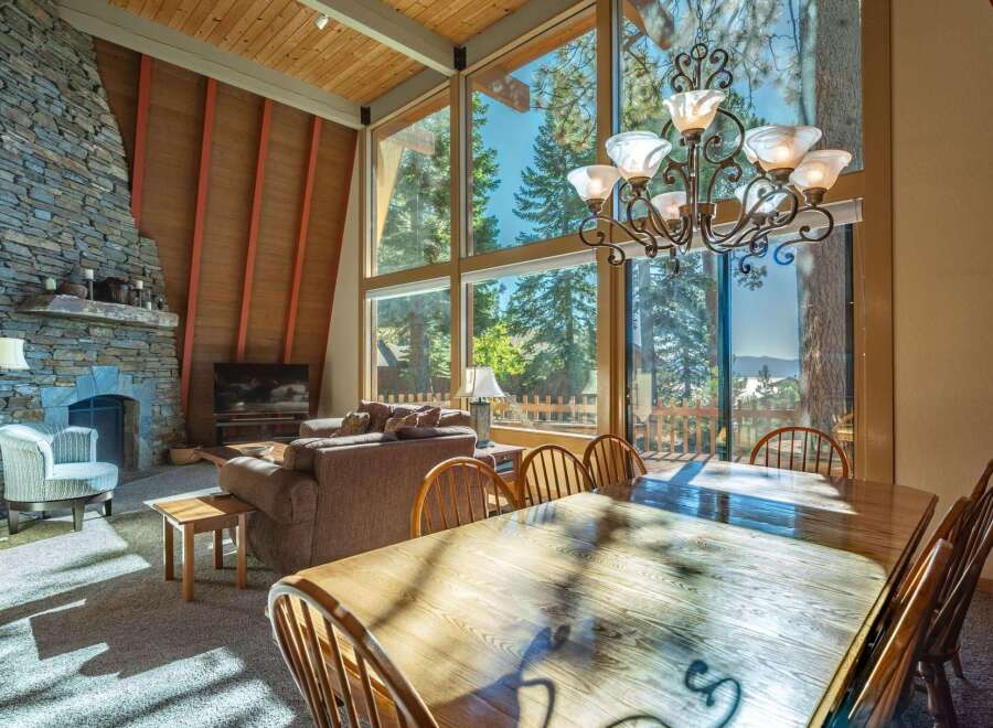Experience breathtaking mountain views from this stunning living and dining area, featuring a grand stone fireplace and soaring vaulted ceilings with exposed wood beams.