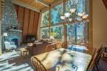 Experience breathtaking mountain views from this stunning living and dining area, featuring a grand stone fireplace and soaring vaulted ceilings with exposed wood beams.