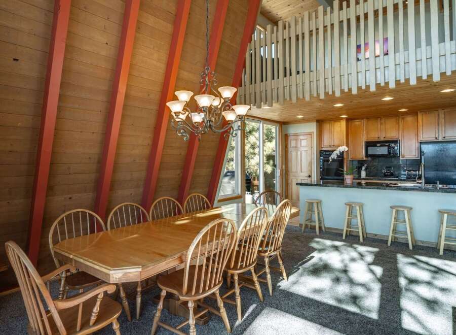 Experience the charm of this A-frame dining area, featuring a spacious wooden table perfect for gatherings, complemented by a striking chandelier.
