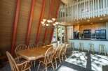 Experience the charm of this A-frame dining area, featuring a spacious wooden table perfect for gatherings, complemented by a striking chandelier.