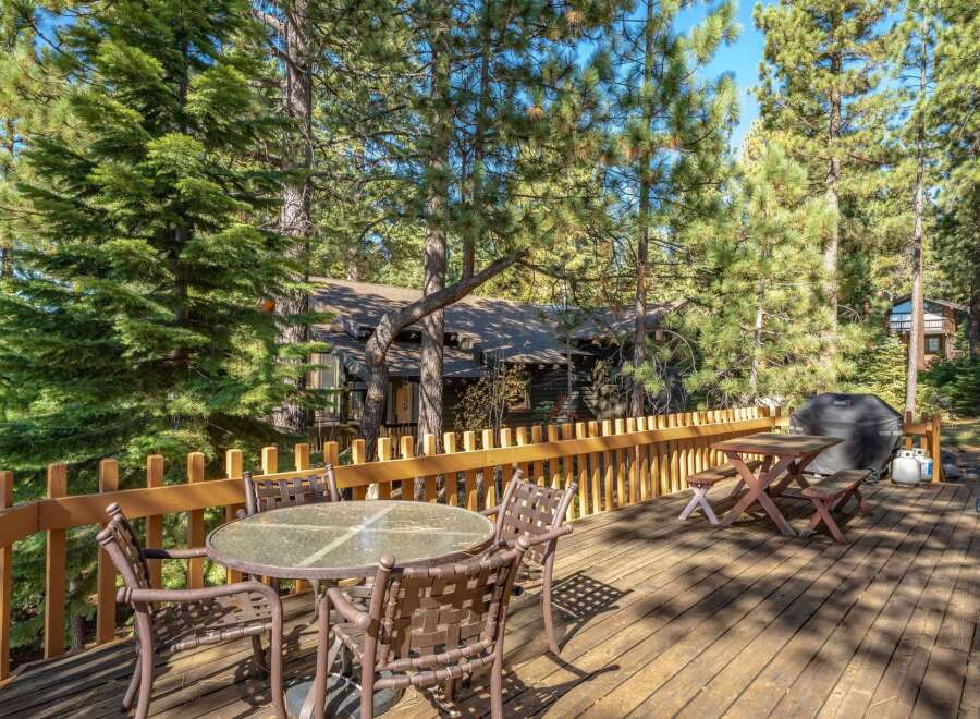Enjoy outdoor living on this spacious wooden deck, perfect for entertaining or relaxing amidst the tall pine trees.