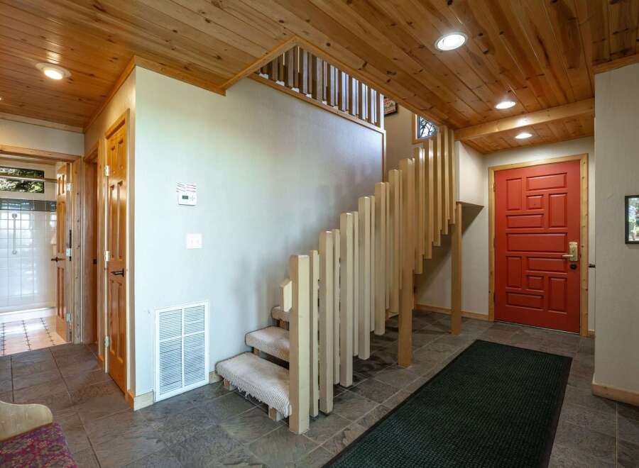 Step into a warm and inviting entryway featuring a striking red front door and a beautiful wooden staircase with a unique slatted railing.
