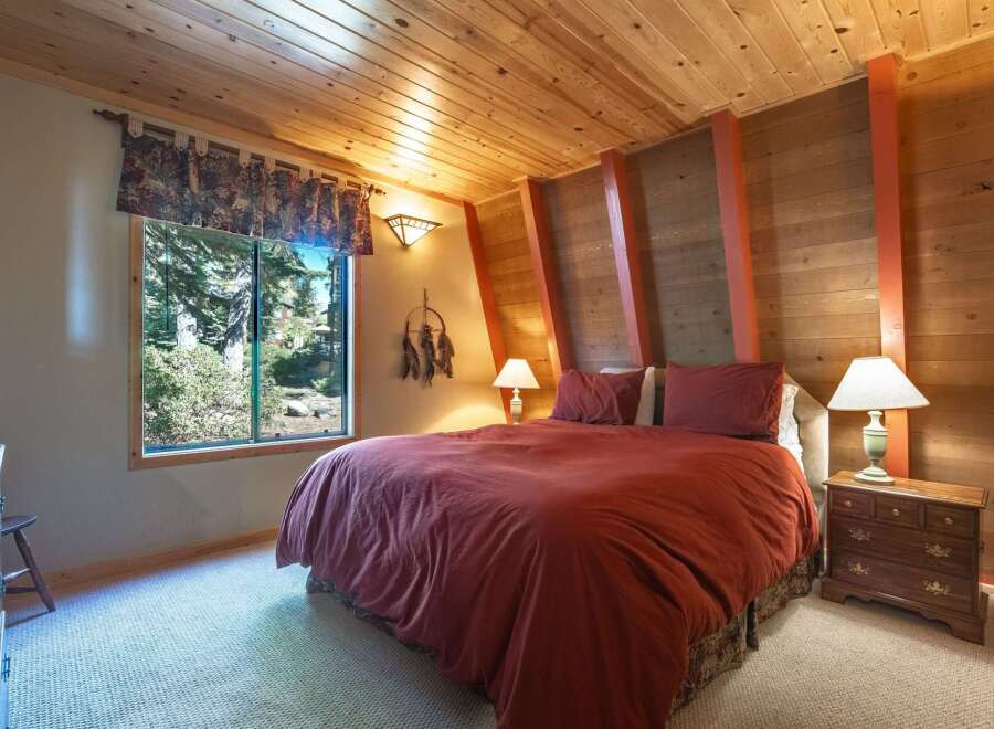 Experience cozy cabin living in this charming bedroom, featuring a rustic wood-paneled ceiling and walls that exude warmth.