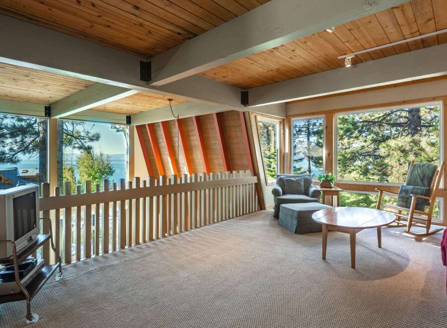Experience breathtaking lake and mountain views from this stunning property, featuring a spacious living area with a vaulted wood-paneled ceiling and exposed beams.