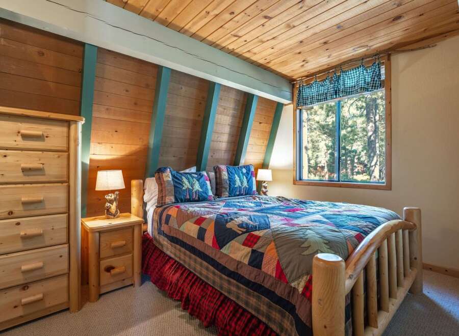 Experience rustic charm in this cozy bedroom, featuring a beautiful log-frame bed adorned with a colorful patchwork quilt and nature-themed pillows.
