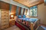 Experience rustic charm in this cozy bedroom, featuring a beautiful log-frame bed adorned with a colorful patchwork quilt and nature-themed pillows.