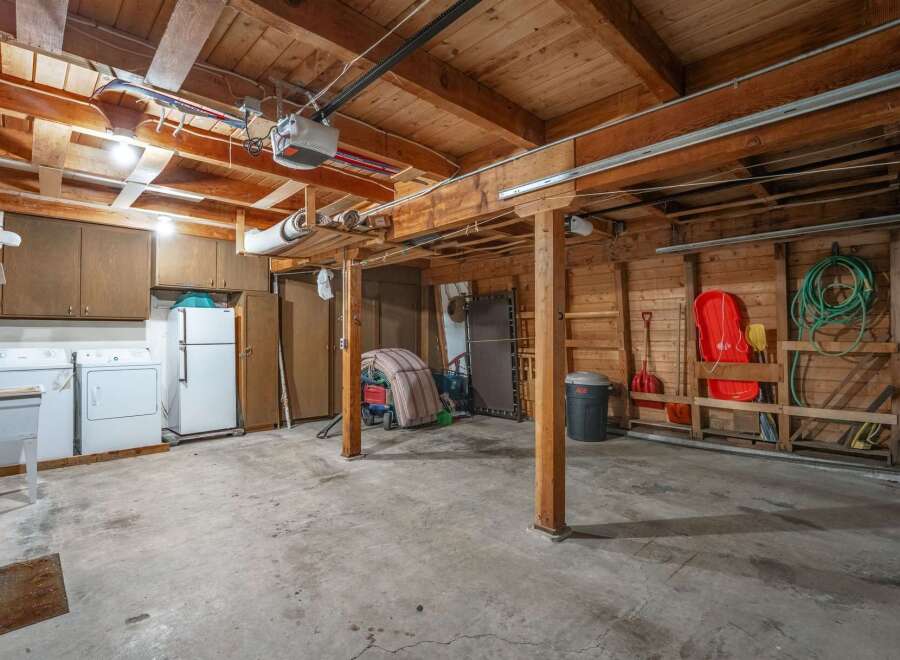 Discover ample storage and functionality in this spacious garage, featuring overhead cabinets and a convenient refrigerator.