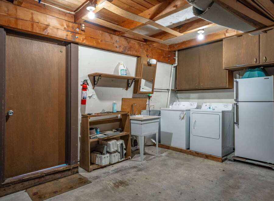 This basement laundry area features a large utility sink, a washing machine, and a dryer, perfect for handling household chores.