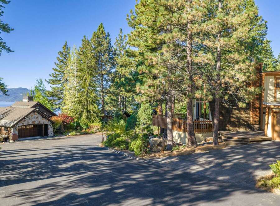 Nestled amongst towering pine trees, this stunning property offers a picturesque setting with a glimpse of a serene lake in the distance.