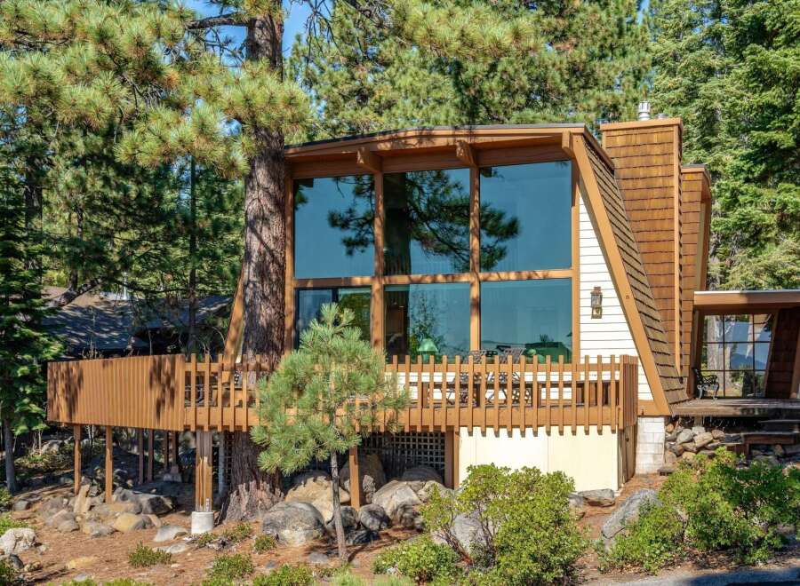 Nestled amongst tall pine trees, this unique A-frame home offers stunning natural views through its expansive floor-to-ceiling windows.