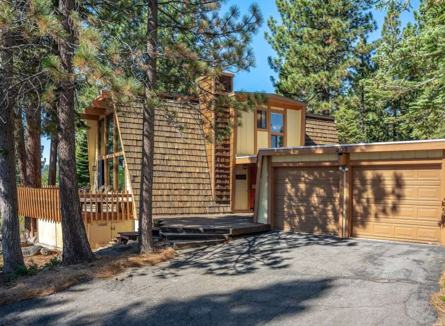 Nestled amongst tall pine trees, this unique A-frame home offers a striking architectural design with its wood shake exterior and expansive windows.