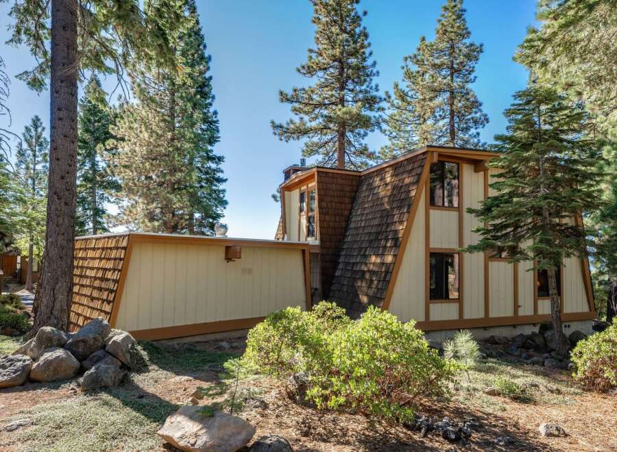 Nestled amongst tall pine trees, this unique A-frame home offers a distinctive architectural style with its angled rooflines and wood shake siding.