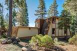 Nestled amongst tall pine trees, this unique A-frame home offers a distinctive architectural style with its angled rooflines and wood shake siding.