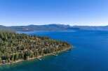 Experience the ultimate lakeside living with this stunning aerial view of homes nestled among pine trees along the crystal-clear waters of Lake Tahoe.