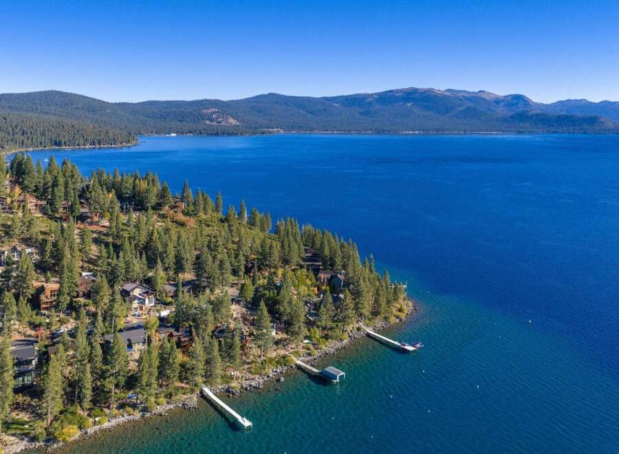 Experience luxury living with this stunning aerial view of lakeside homes nestled among tall pine trees.