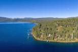 Experience luxury living with this stunning aerial view of waterfront properties nestled among lush pine trees on a hillside overlooking a vast, deep blue lake.