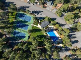 Experience resort-style living with this stunning aerial view showcasing multiple pristine tennis courts and a sparkling blue swimming pool.