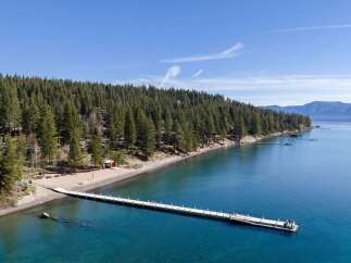 Experience luxury lakeside living with this stunning aerial view of a private pier extending into crystal-clear blue waters.