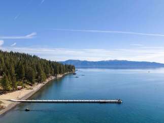 Experience serene lakefront living with this stunning property featuring a private beach and a long, white pier extending into crystal-clear blue waters.