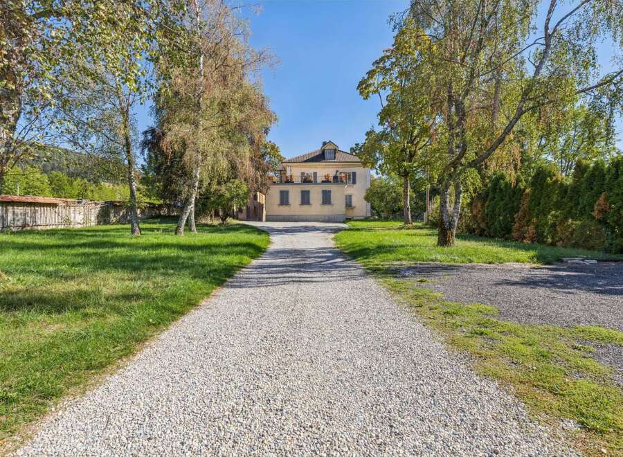 Discover this charming property featuring a stately yellow house with a prominent balcony and multiple windows, accessed by a long gravel driveway.