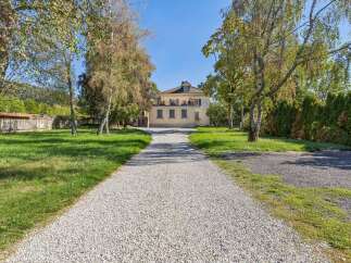 Discover this charming property featuring a stately yellow house with a prominent balcony and multiple windows, accessed by a long gravel driveway.
