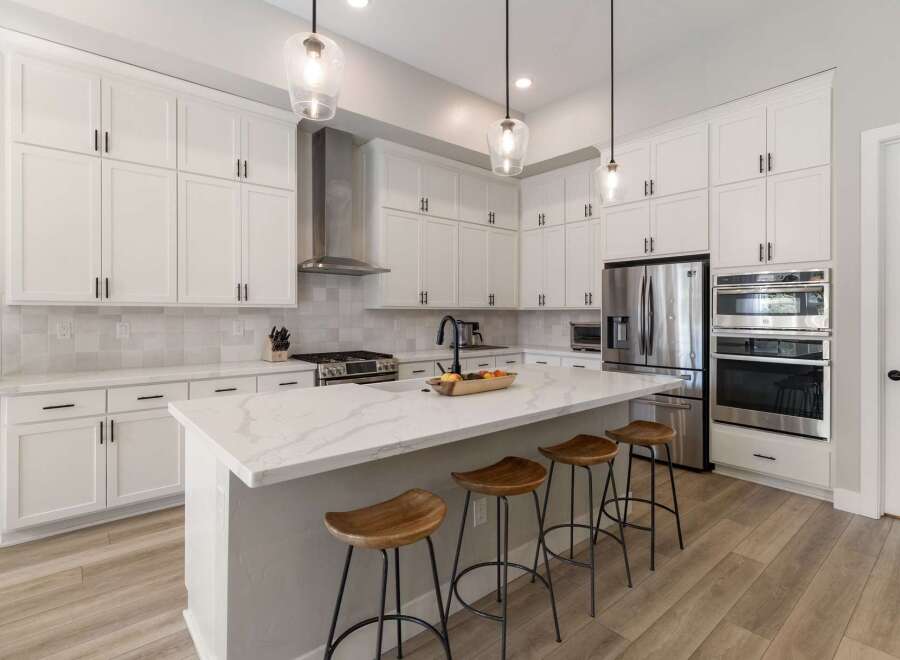 Experience modern luxury in this stunning white kitchen, featuring sleek cabinetry, a spacious quartz island with bar seating, and top-of-the-line stainless steel appliances.