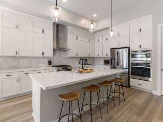 Experience modern luxury in this stunning white kitchen, featuring sleek cabinetry, a spacious quartz island with bar seating, and top-of-the-line stainless steel appliances.