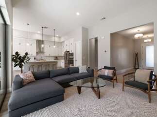 Experience modern living in this open-concept home featuring a sleek white kitchen with a large island and pendant lighting, seamlessly flowing into a spacious living area.