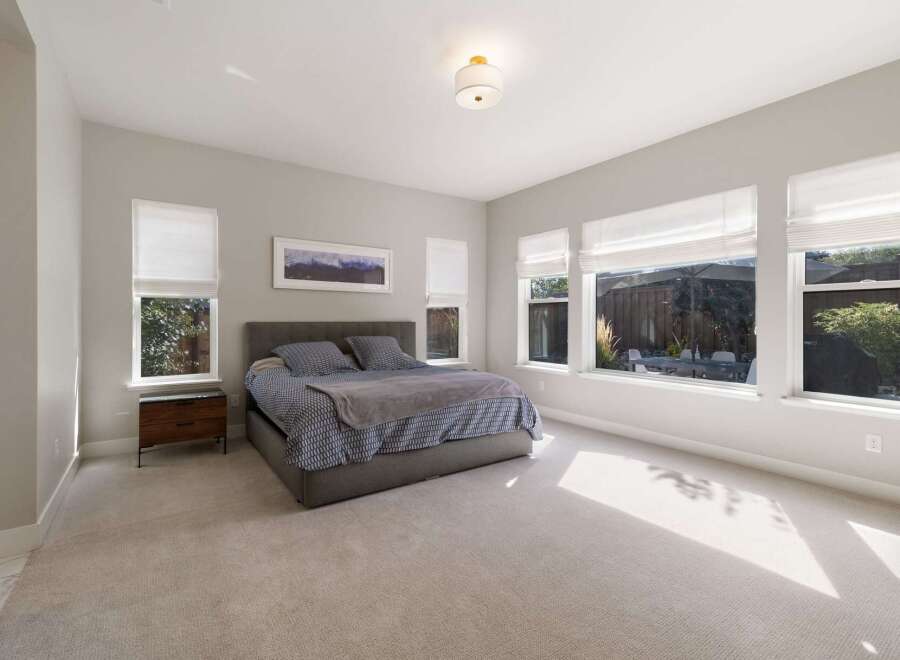 Experience luxurious comfort in this spacious master bedroom, featuring a king-size bed with a stylish upholstered headboard and a plush, neutral carpet.