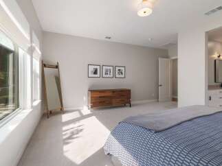 This spacious bedroom features a large window with abundant natural light, a stylish wooden dresser, and a full-length mirror.