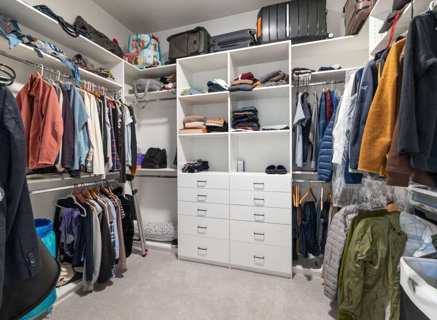 Discover ample storage in this spacious walk-in closet, featuring custom shelving and multiple hanging rods to organize your wardrobe.