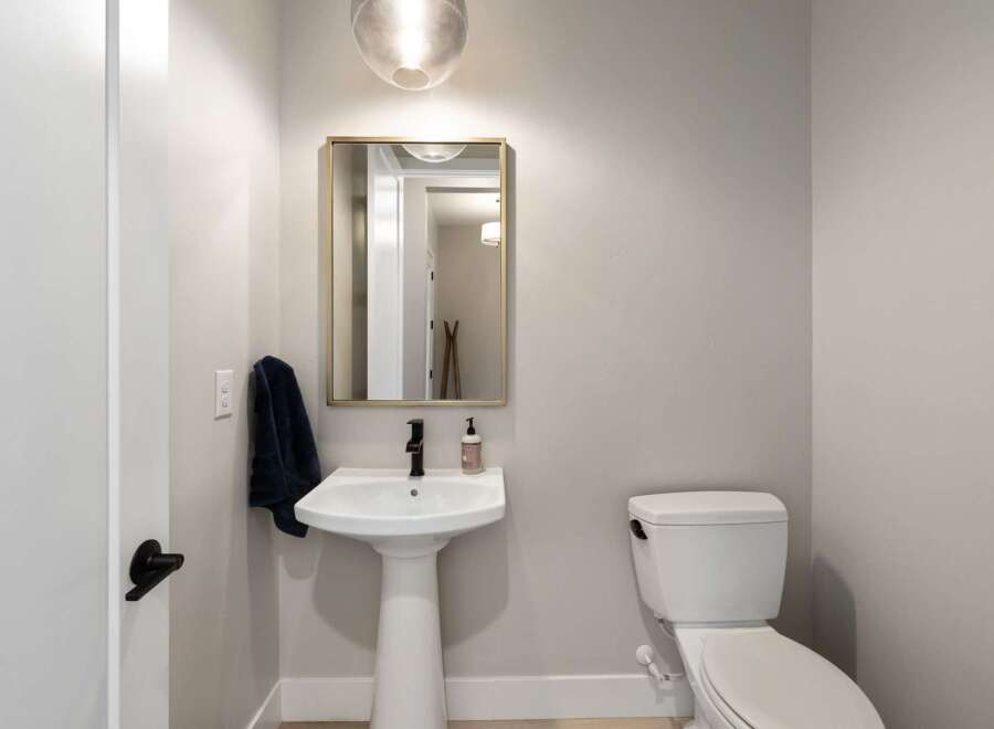 This modern powder room features a sleek pedestal sink with a black faucet, complemented by a gold-framed mirror and a stylish pendant light.