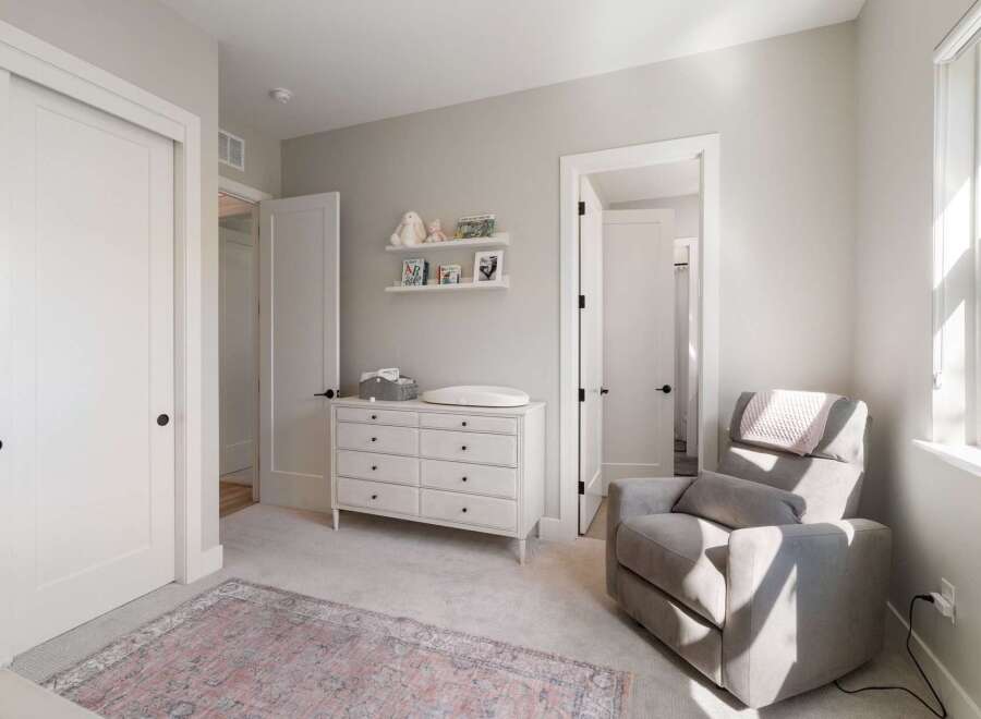 This charming nursery features a comfortable gray recliner with a pink throw, perfect for soothing a baby.