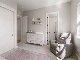 This charming nursery features a comfortable gray recliner with a pink throw, perfect for soothing a baby.