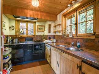 Experience rustic charm in this cozy kitchen, featuring a classic black range and a double sink set against a stunning red granite countertop.
