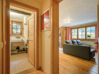 Step into a charming living space featuring a comfortable grey sofa perfect for relaxation, complemented by large wooden-framed windows that offer scenic views.