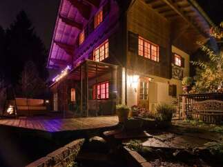 Experience the magic of this charming chalet at night, illuminated by warm interior lights and festive string lights.