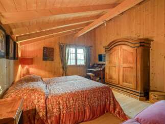 Experience rustic charm in this cozy bedroom featuring warm wooden walls and a vaulted ceiling with exposed beams.