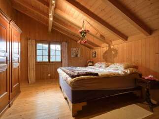 Experience rustic charm in this cozy wooden bedroom, featuring a comfortable bed adorned with floral linens and a warm, inviting atmosphere.