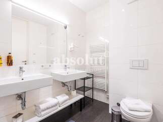 Experience modern comfort in this pristine bathroom, featuring two sleek white sinks and a wall-mounted toilet with a dual-flush system.