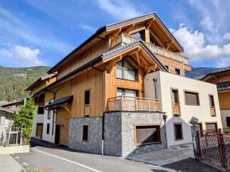Experience modern alpine living in this stunning wooden chalet, featuring a striking stone base and multiple balconies offering breathtaking mountain views.