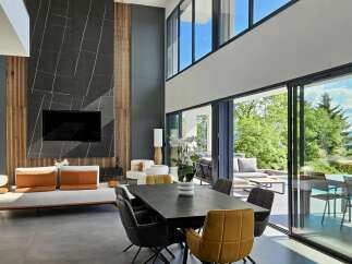 Experience modern luxury in this spacious living and dining area, featuring a dramatic floor-to-ceiling dark stone fireplace with vertical wood accents.