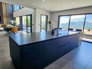 Experience luxury living in this modern open-plan kitchen and dining area, boasting a sleek dark island with an integrated cooktop and stunning panoramic mountain views through expansive sliding glass doors.