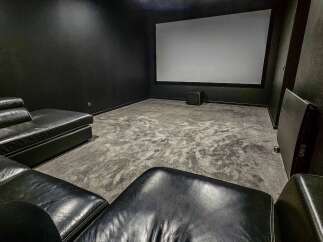 Experience cinematic bliss in this dedicated home theater, featuring a massive projection screen and plush black leather seating for ultimate comfort.